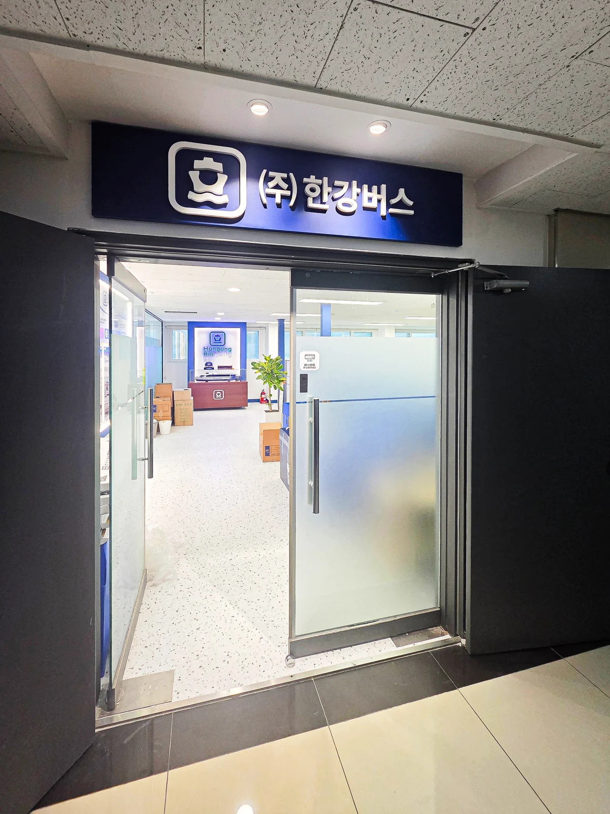 복도에서 본 사무실 출입문 위 회사 사인과 문 안쪽의 로고 전시대