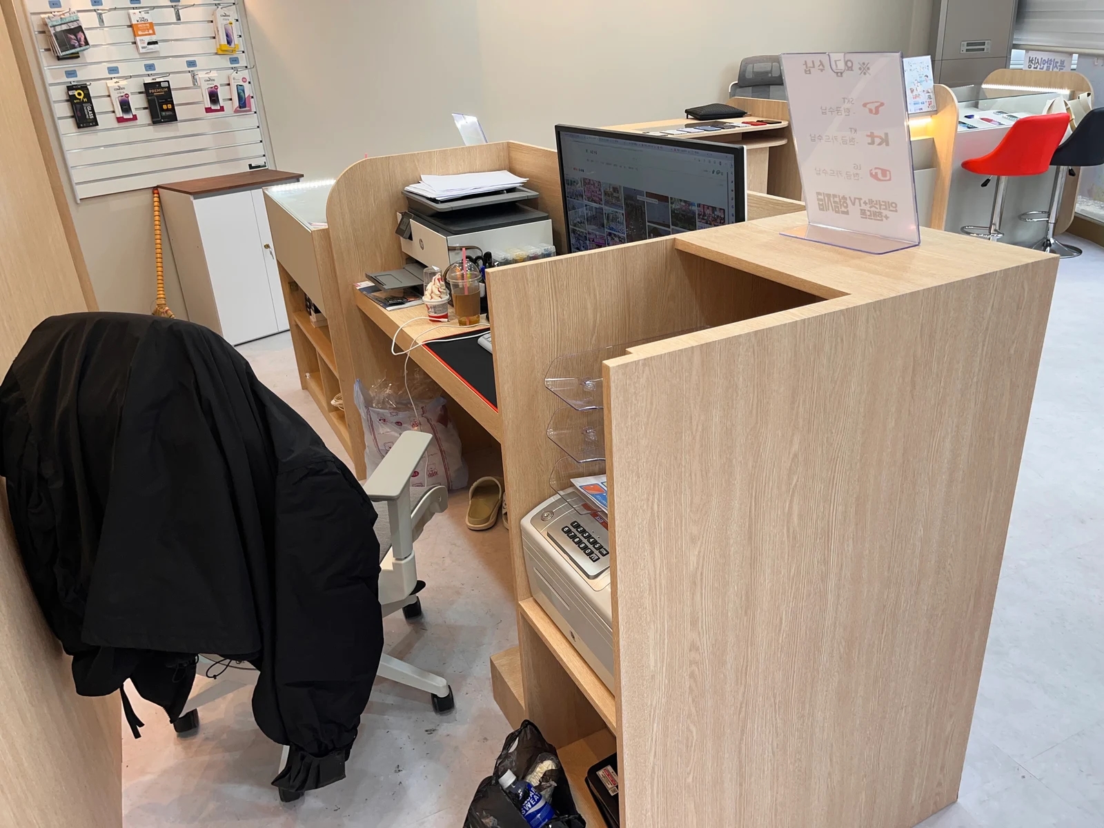 가림판 안쪽에 모니터와 출력 기기, 서류와 작은 선반이 놓인 휴대폰 매장 업무석
