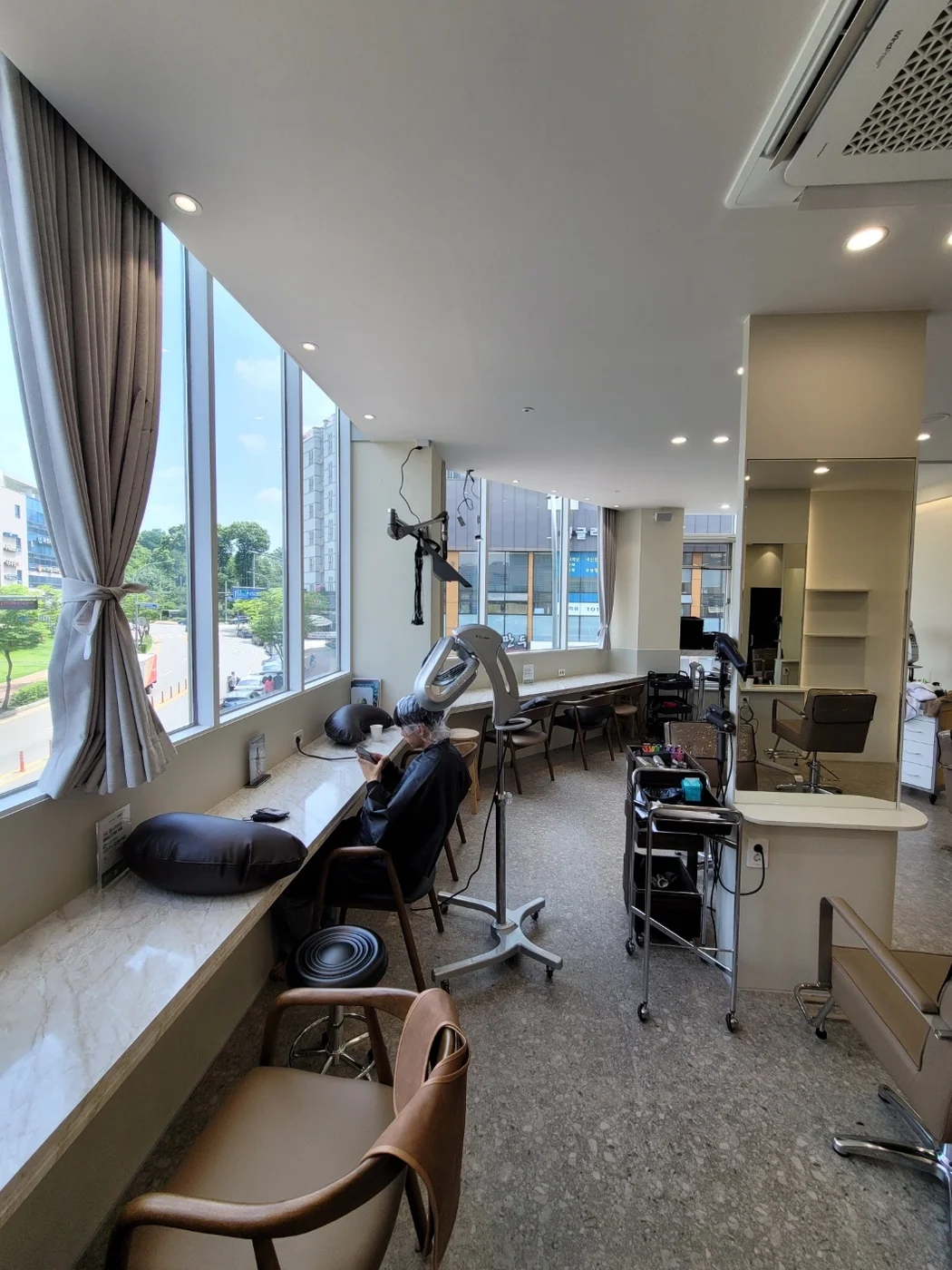 창가의 나무색 긴 테이블과 밝은 벽이 있는 미용실